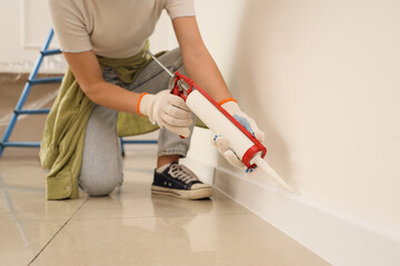 Young woman applying sealant to baseboard in room