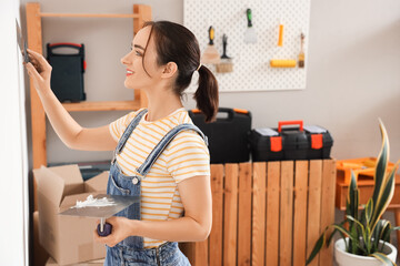 Young woman with putty knives near wall in room