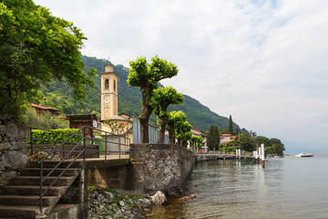 Lakefront walkway, dock and church in Vassena on Lake Como, Italy.