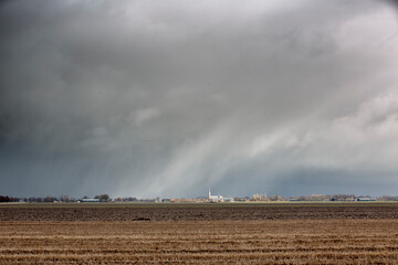 Dark storm clouds loom over a rural landscape near a small town with fields and distant buildings