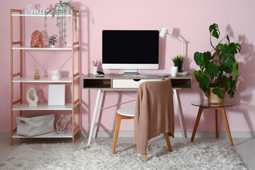 Modern workplace with computer and stationery near pink wall in room