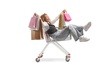 Asian woman sitting inside a shopping cart and holding shopping bags