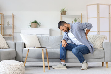 Young man suffering from back pain on sofa at home