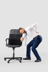 Young businessman suffering from back pain near chair on light background