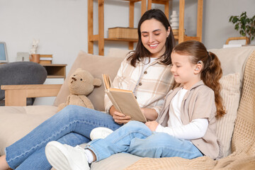 Little girl with hearing aid and her mother reading book on sofa at home