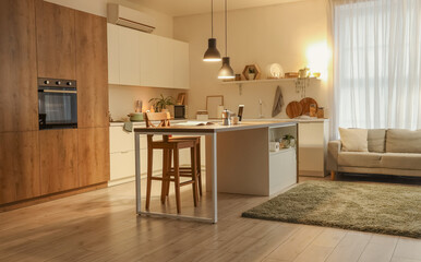 Interior of kitchen with sofa, counters and glowing lamps in evening