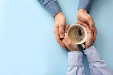 Hands of couple with coffee cup on blue background, top view