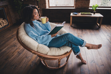 Young woman enjoying a relaxing day at home, reading a book and sipping coffee in a cozy living...