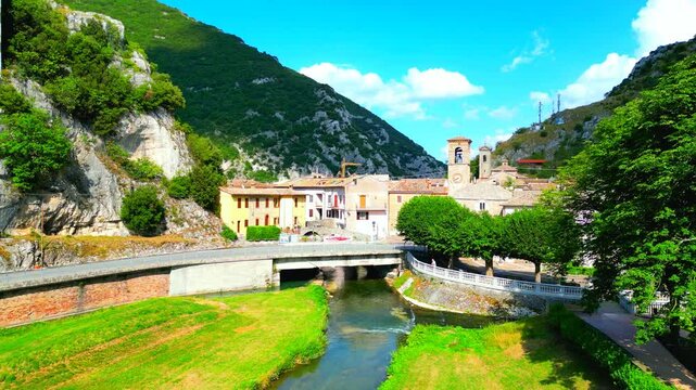 Establishing aerial pullback pedestal up shot of the Pioraco town center, with the sumptuous Potenza River, adorning greenery, road and bridge, town hall, cloister and belltowers, buildings, Sibillini