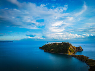 Blue skies with a bit of clouds over a vast tropical ocean and a rocky mountain