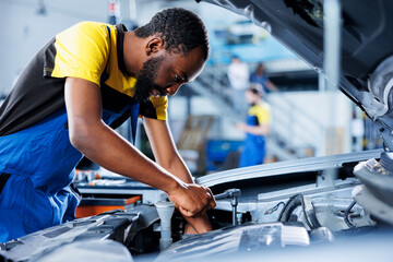African american repairman in car service uses torque wrench to tighten bolts after replacing...