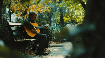Elderly man plays acoustic guitar on park bench in autumn.
