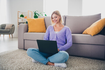 Young woman enjoying her weekend indoors, relaxing with her laptop in a cozy living room setup.