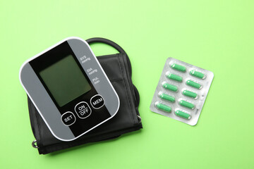 Blood pressure measuring device and pills on green background, top view