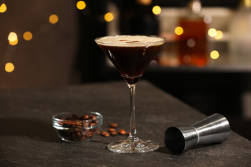 Glass with delicious espresso martini, coffee beans and jigger on table in bar