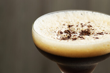 Delicious espresso martini with coffee beans in glass on blurred background, closeup