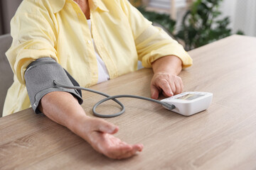 Senior woman measuring blood pressure at wooden table indoors, closeup