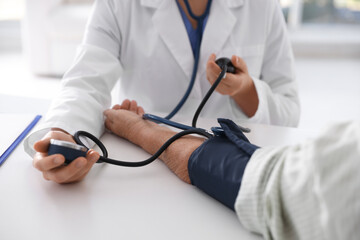 Doctor measuring patient's blood pressure at table in hospital, closeup
