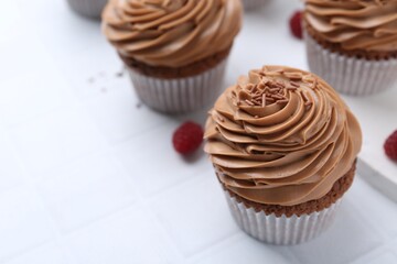 Tasty cupcakes with chocolate cream and raspberries on white tiled table, closeup. Space for text