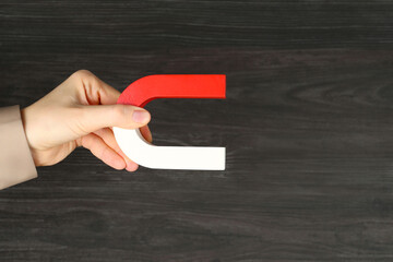 Woman with horseshoe magnet on wooden background, closeup