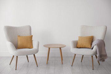 Soft armchairs and coffee table near white wall indoors