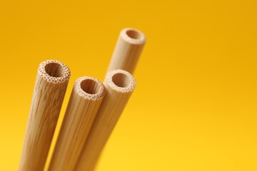 Bamboo drinking straws on yellow background, closeup. Space for text
