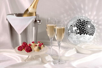 Champagne in glasses, ice bucket with bottle and tasty candies on white fabric