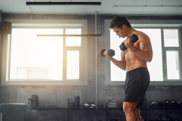 A dedicated man is lifting dumbbells in a bright and vibrant gym environment, showcasing fitness...