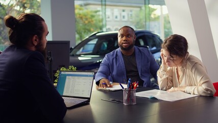 Customers negotiating correct price and financing options after finding right vehicle for them in showroom and deciding to buy it. Dealership clients reading contract terms and conditions, camera B