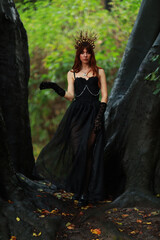Fototapeta premium Young witch with crown on her head in the forest