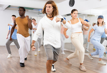 Fototapeta premium Group of sportive young adult diverse dancers performing dynamic movements during aerobic dance workout in gym