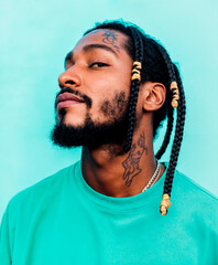 Confident  dominican  black man with braided hair, tattoos, and turquoise shirt on a blue background.  .