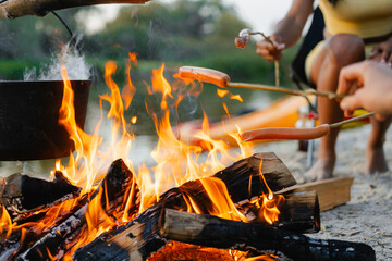 Friends roast sausages over a campfire