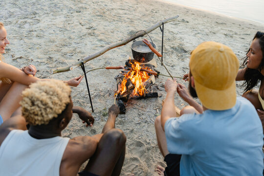 Friends roast sausages over a campfire
