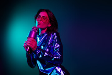 Portrait of stunning young woman sing mic empty space wear shiny dress neon light dark blue...