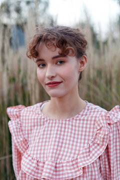 woman wearing a pink gingham blouse stands in tall grass