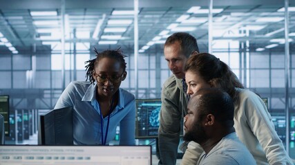 Multiethnic team of engineers working in server hub, using PCs to analyze data. Multiracial group of employees examining infrastructure in data center, ensuring system integrity and security, camera A