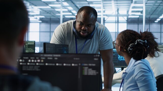 Manager doing team meeting with engineers, delegating tasks in high tech data center office. Supervisor doing brainstorming with IT experts how to while monitor AI supercomputers, camera A