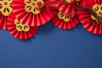 Bright red paper fans with intricate gold flower patterns on a deep blue background. Chinese New...