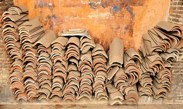 Rome, Italy - December 2, 2024: A stack of traditional terracotta roof tiles neatly arranged against an aged wall with visible textures, highlighting Italian architectural heritage