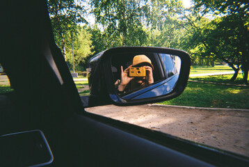 Anonymous woman in yellow cap capturing a photo in the mirror of a car