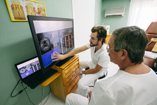 Two dentists looking at a 3D model of human jaw on a screen