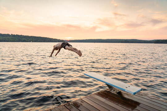 Teen Boy Diving into Lake from Cottage Dock at Sunset