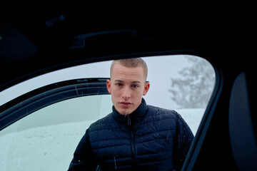 A young man standing by a car in a snowstorm