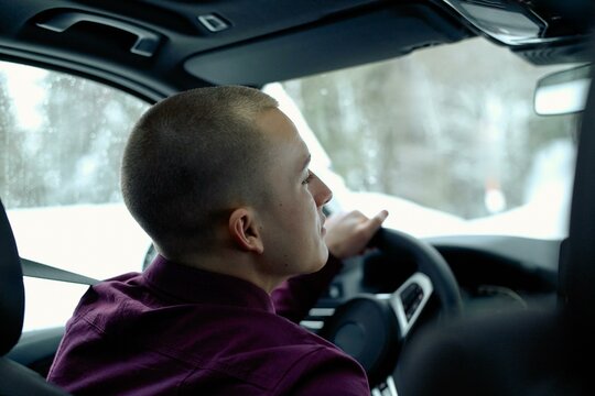 Young man driving through a snowy forest road