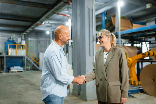 A man and a woman shake hands in a factory