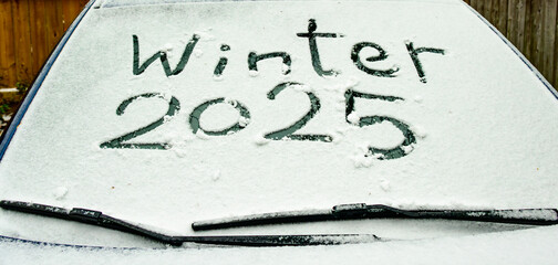Winter 2025 written by a finger on the windsheild of a car covered with white ice and snow
