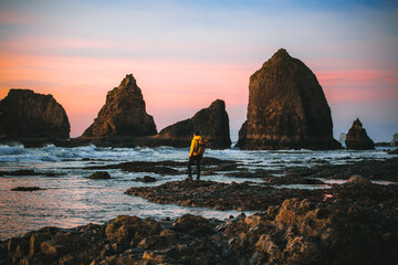 A man with a backpack in yellow jacket admires a beautiful sunset at Oceanside Beach, Oregon