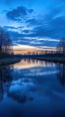 Fototapeta premium Tranquil river at dusk reflecting a serene blue sky and trees.