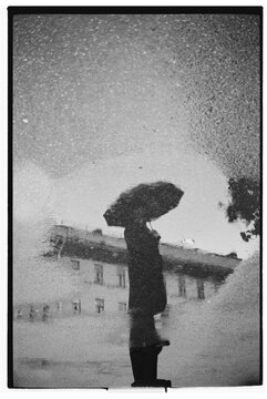 Reflection of a person holding an umbrella in a puddle on a rainy day
